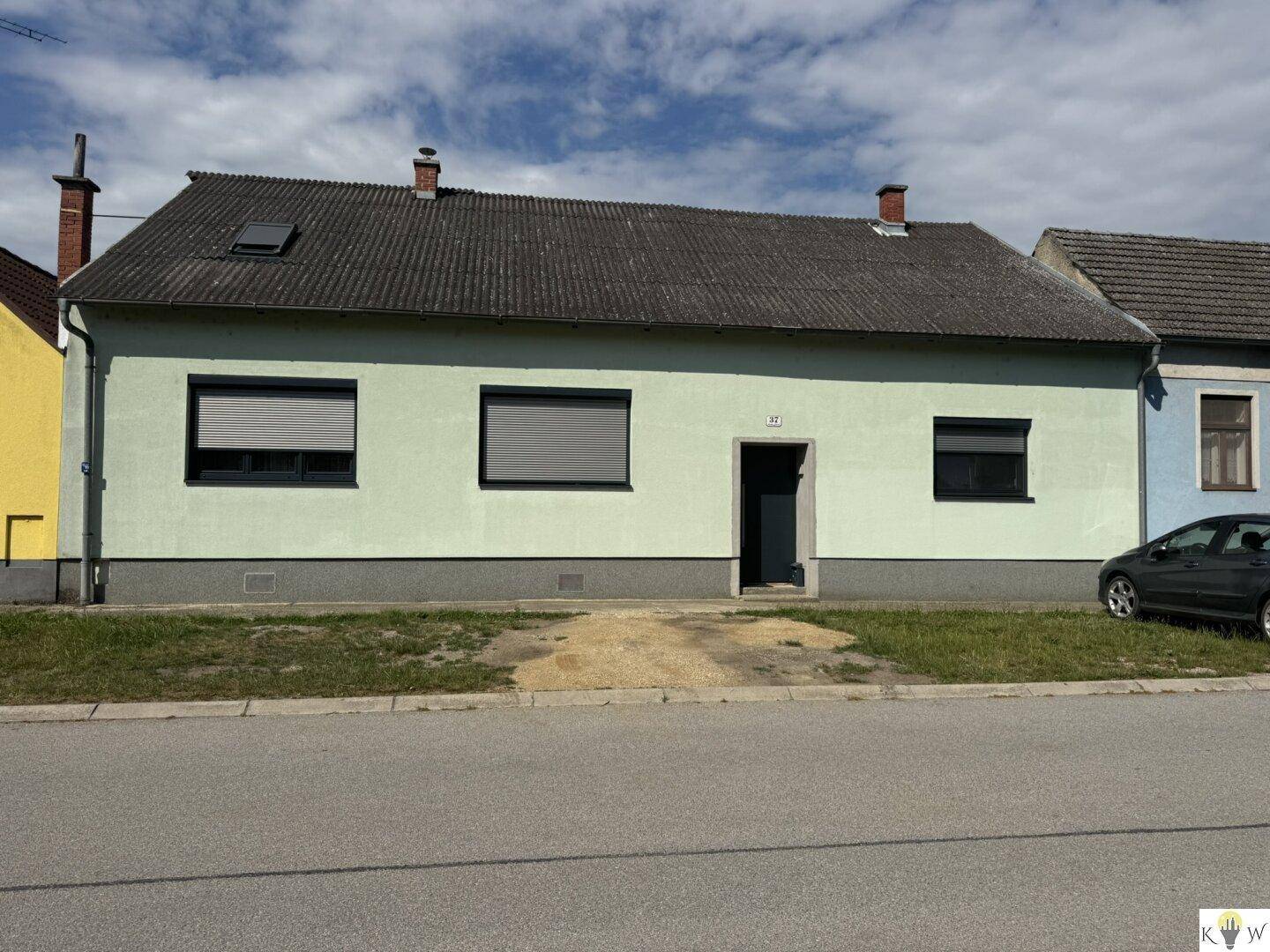Vorderansicht eines Einfamilienhauses mit hellgrüner Fassade und Rollläden an den Fenstern.