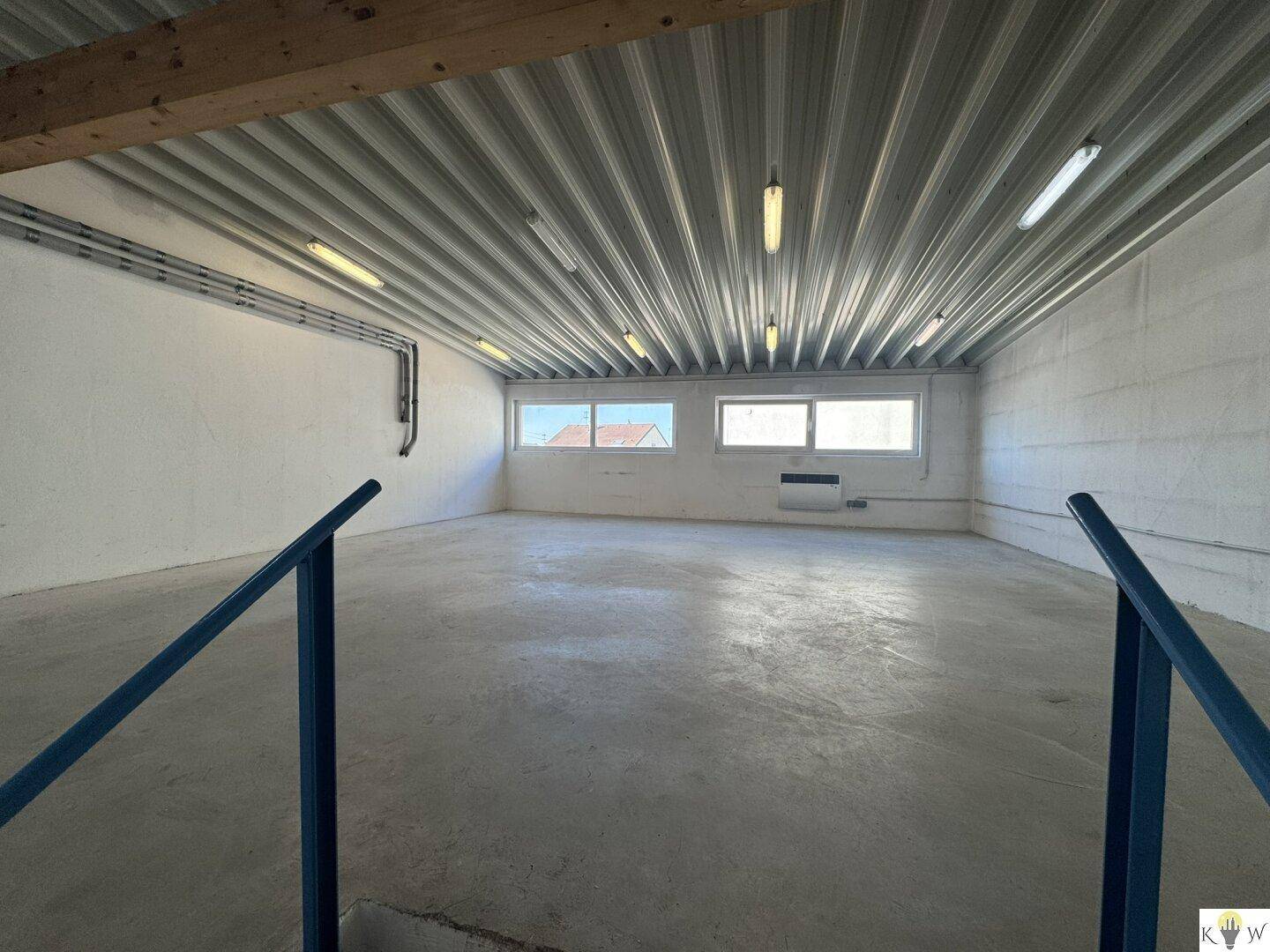 Leerer Lagerraum mit Betonboden, hohen Decken und Fenstern für Tageslicht.