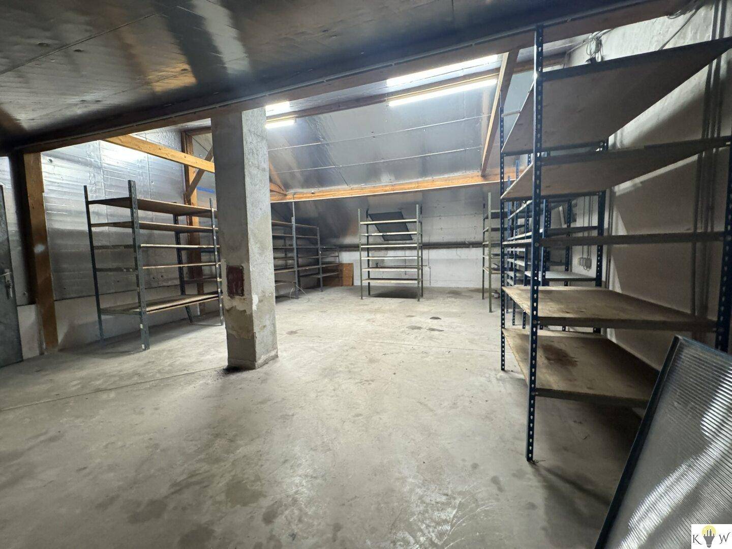 Großer Lagerraum mit Regalen, Betonboden und Oberlichtern für natürliche Beleuchtung.