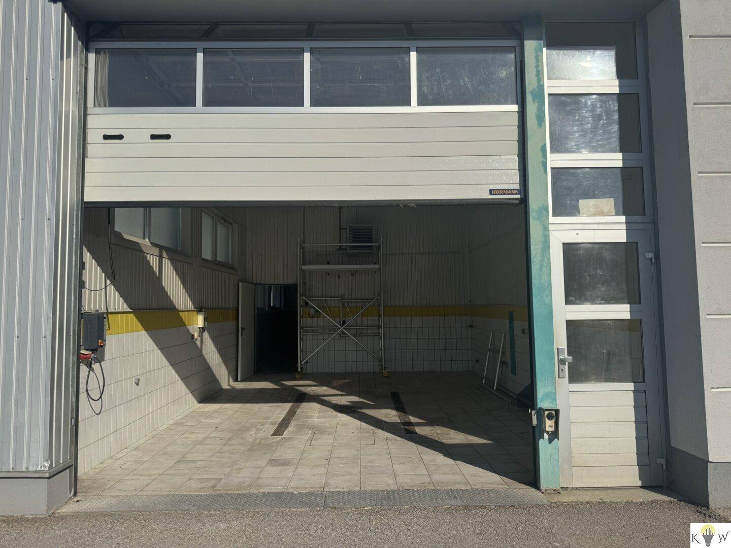 Großer Werkstattbereich mit offenem Garagentor, Fliesenboden und viel Tageslicht.