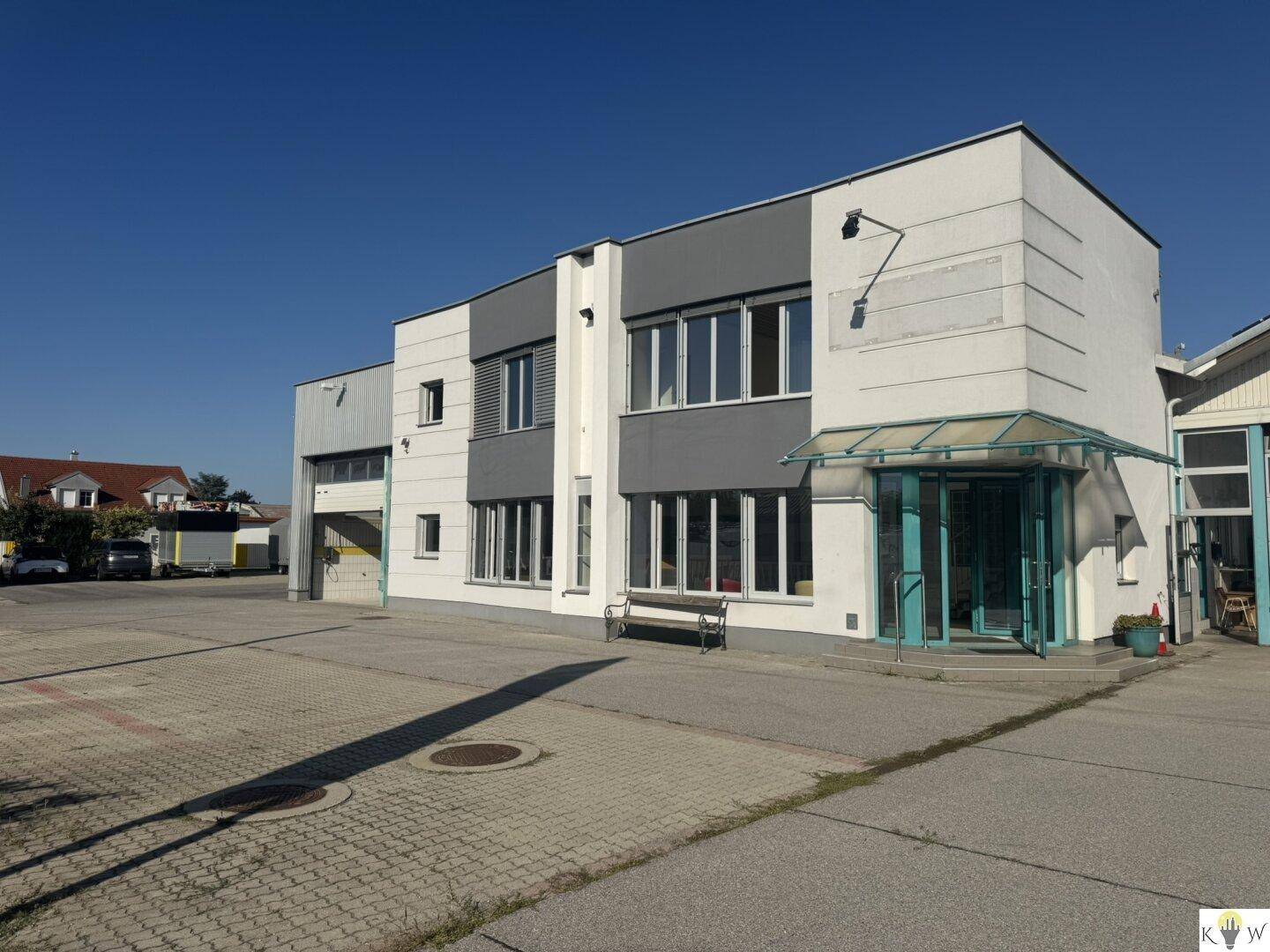 Ansicht des Geschäftsgebäudes mit Eingangsbereich und großem Parkplatz davor.