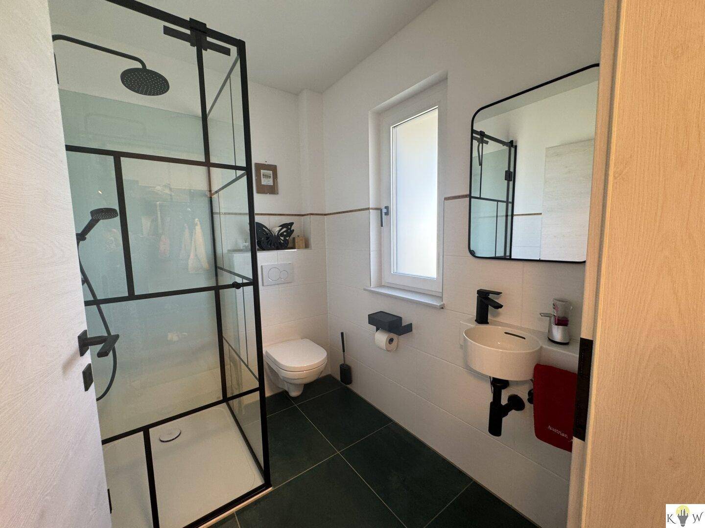Modernes Gäste-WC mit dunklen Bodenfliesen, Duschkabine und kleinem Waschbecken.