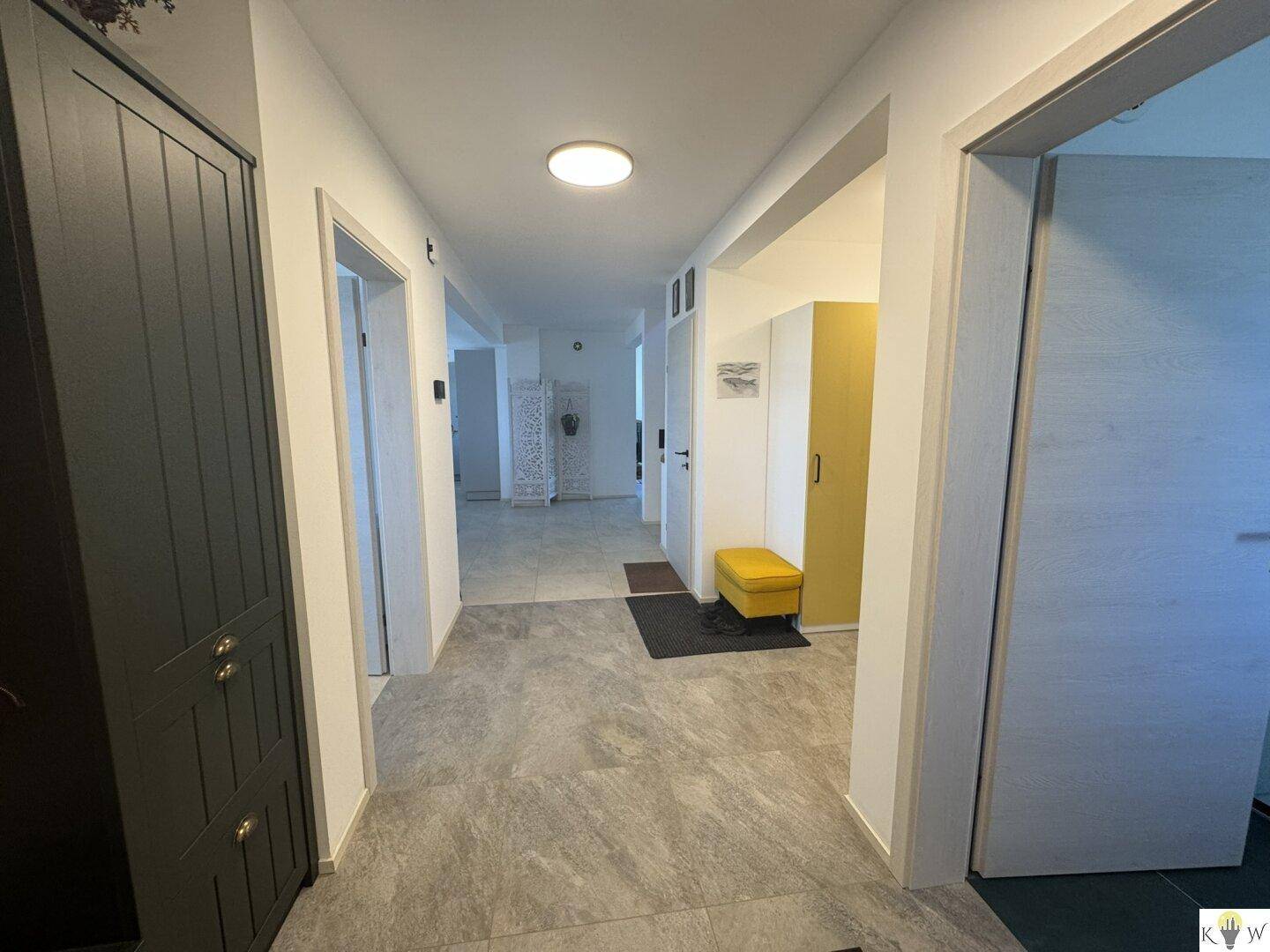 Heller Flur mit modernen grauen Fliesen, Garderobenschrank und Zugang zu weiteren Räumen.