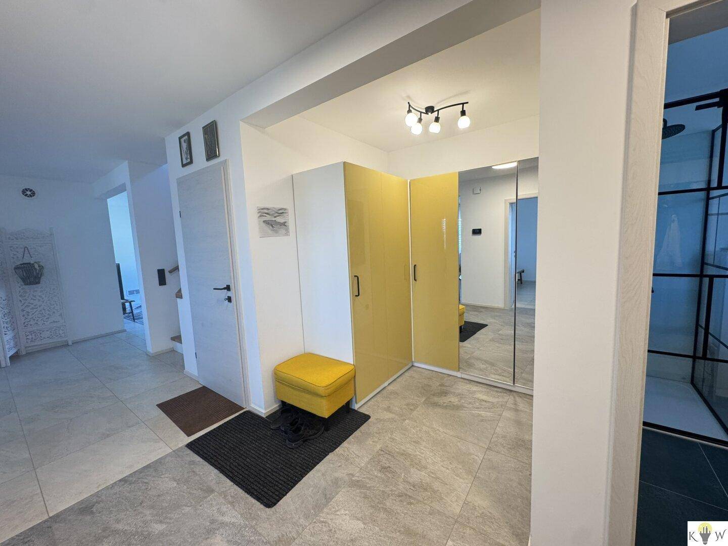 Eingangsbereich mit großem Spiegelschrank, gelber Sitzbank und modernen Fliesenboden.