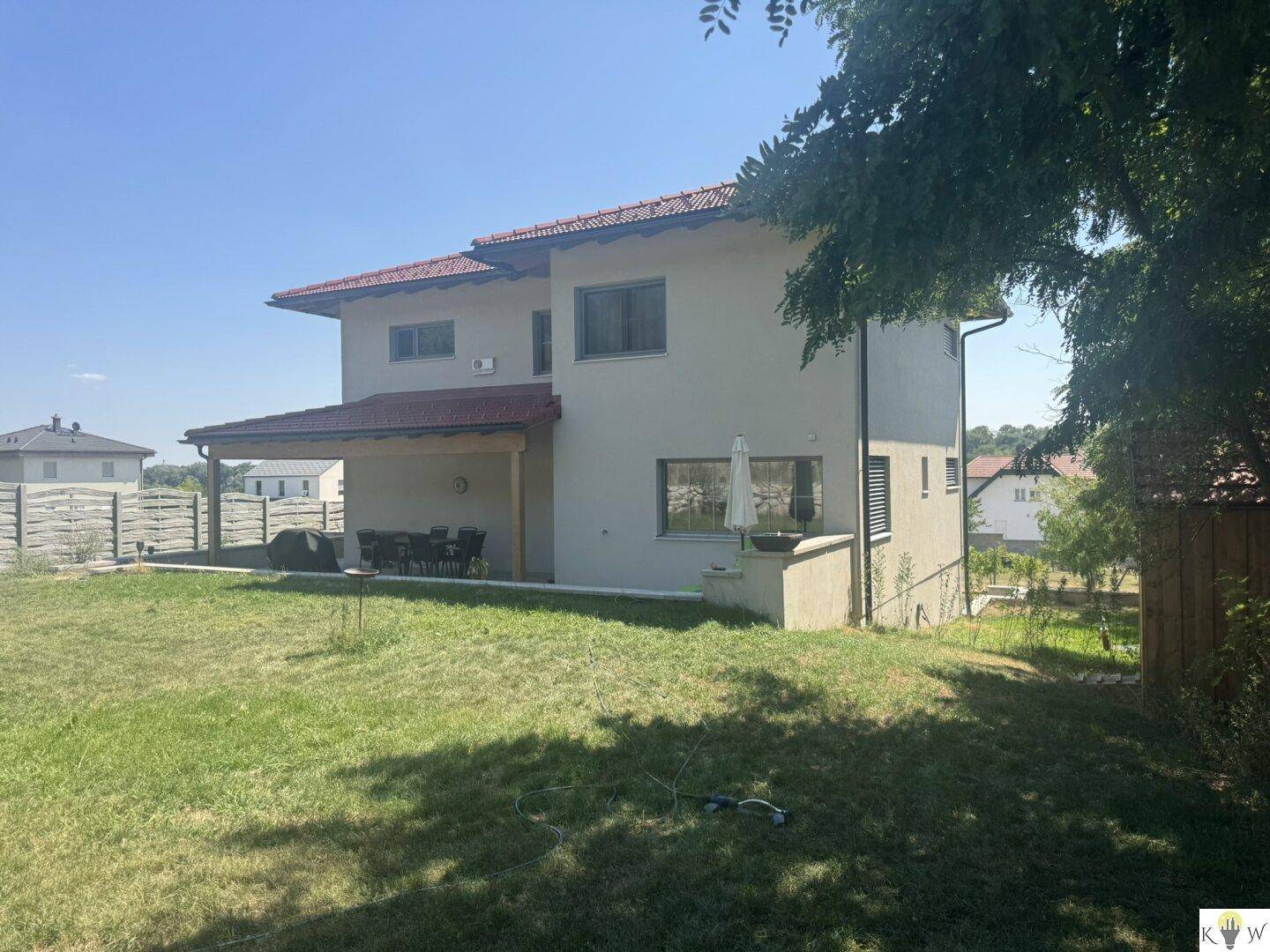 Rückansicht des Hauses mit überdachter Terrasse, Gartenmöbeln und großem Rasenbereich.