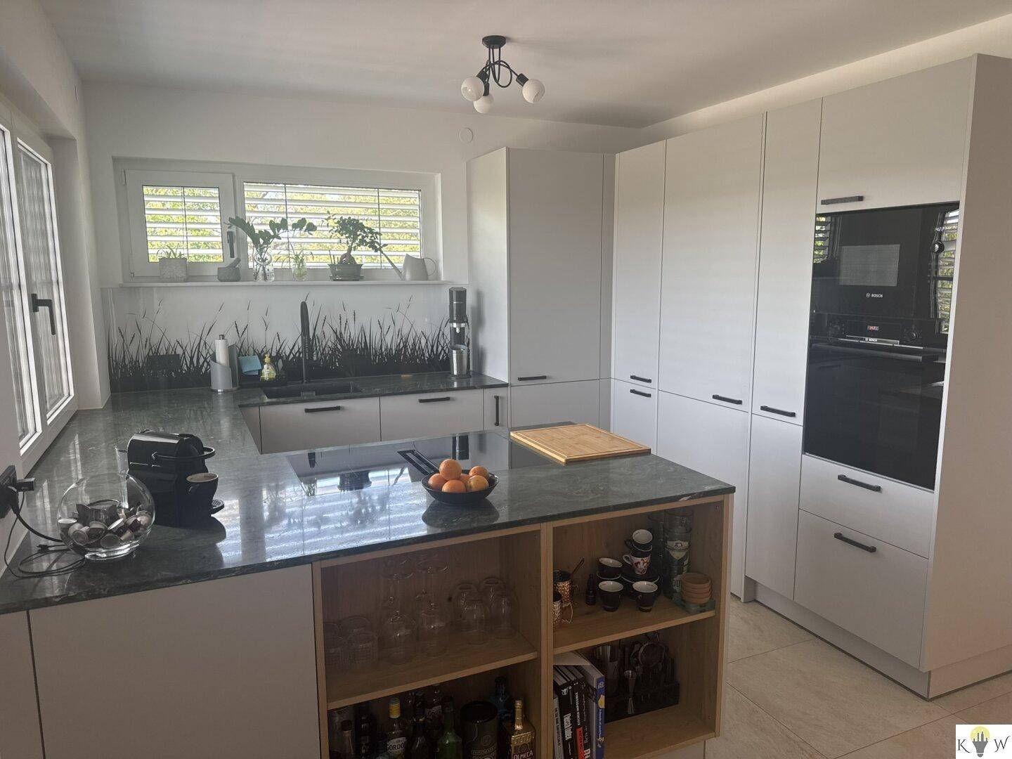 Helle Einbauküche mit Kücheninsel, Backofen und viel Stauraum in den Schränken.