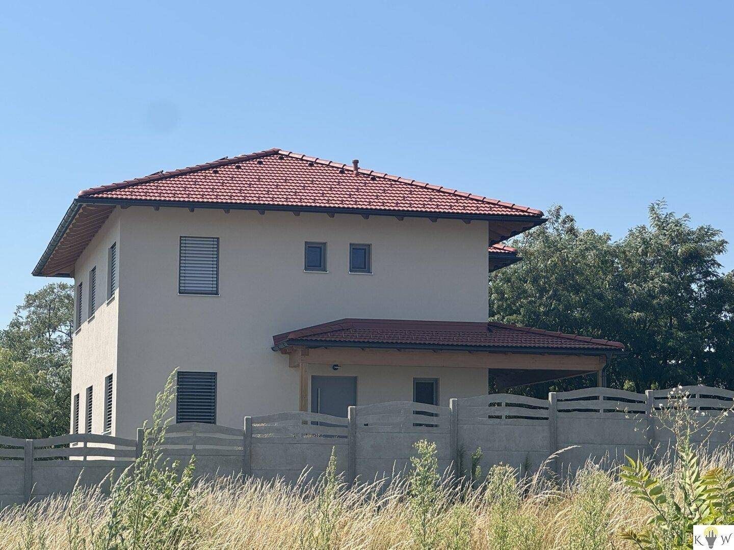 Seitenansicht des modernen Hauses mit rotem Ziegeldach und einem Sichtschutzzaun im Vordergrund.