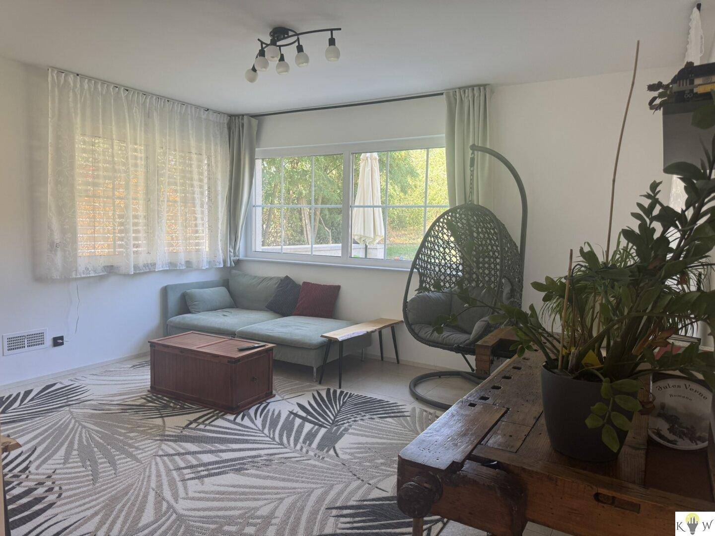 Gemütliches Wohnzimmer mit Sofa, Teppich und Blick in den Garten durch große Fenster.
