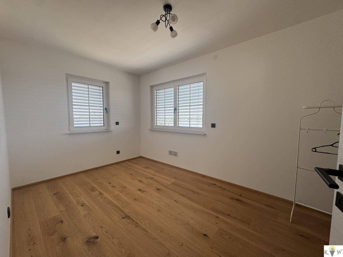 Helles Schlafzimmer mit Holzboden und zwei Fenstern, bereit zur individuellen Gestaltung.