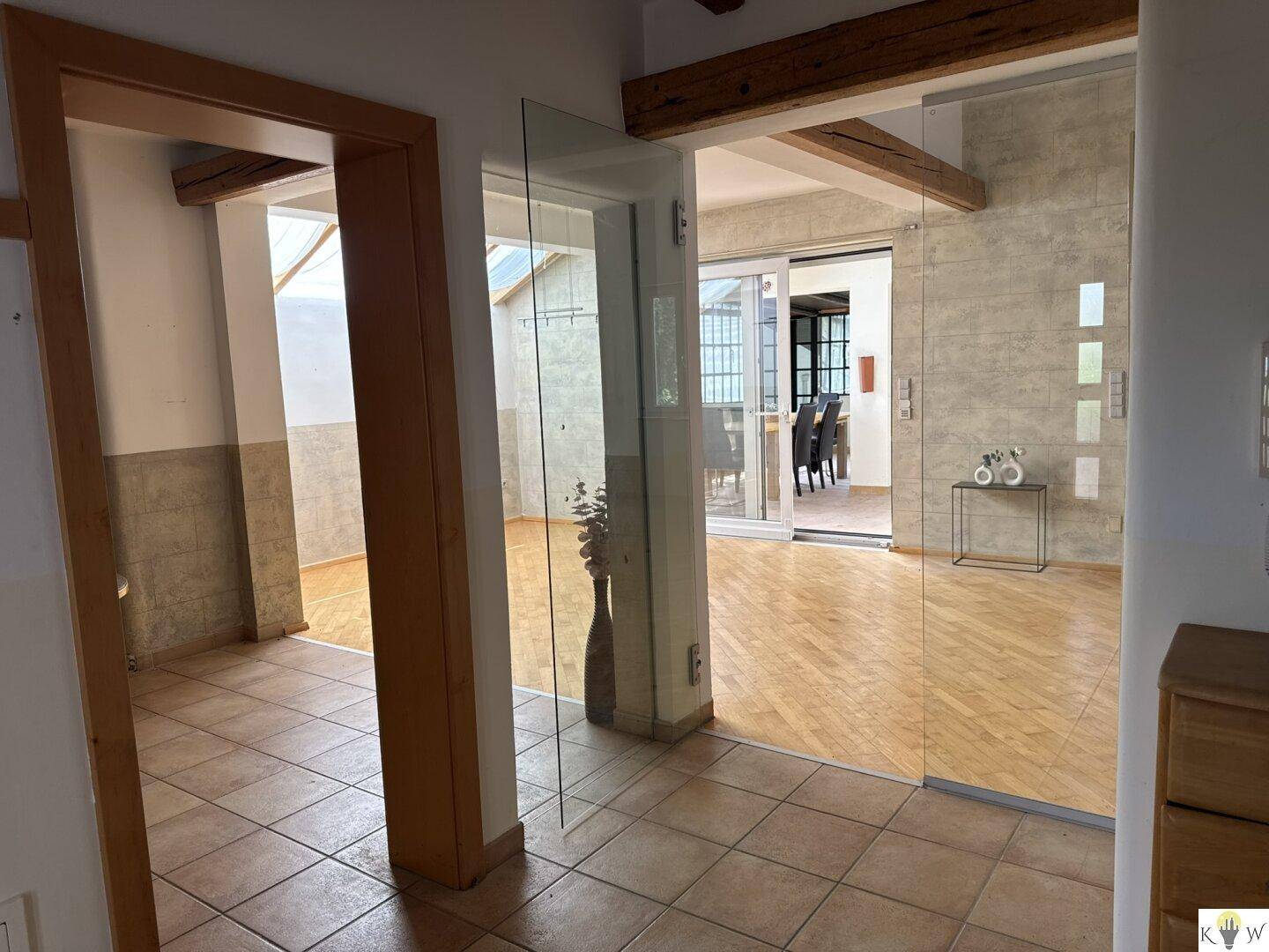 Heller Flur mit Fliesenboden, Holzbalken und Glaswänden, die den Blick in angrenzende Räume freigeben.