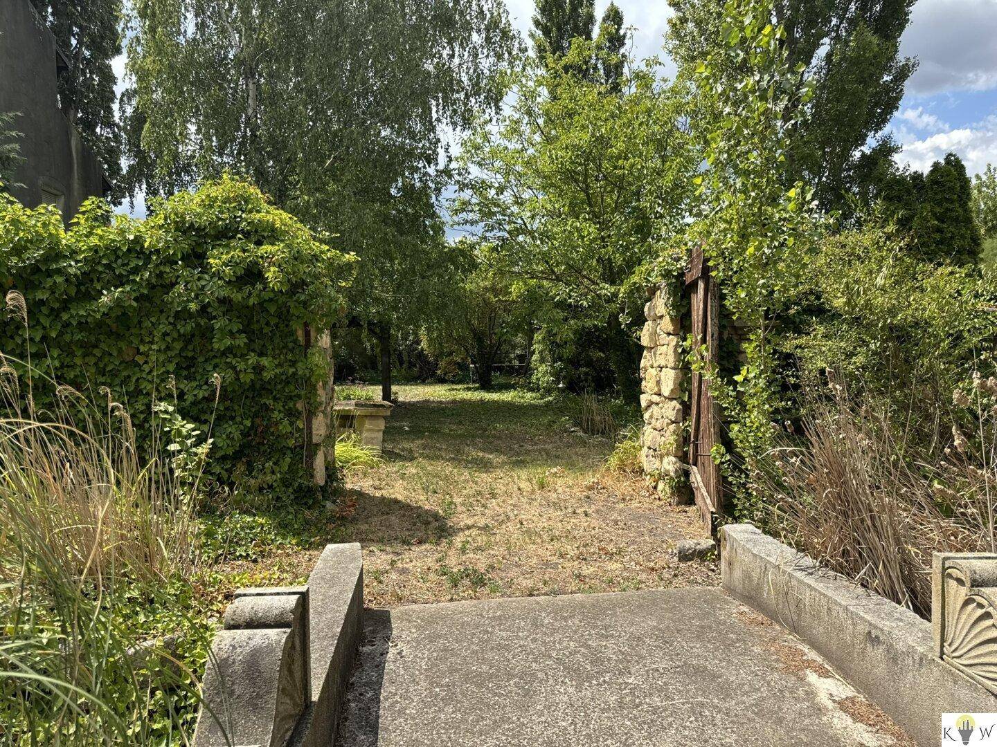 Eingangsbereich zum weitläufigen Garten mit Steinmauern und üppiger Vegetation, führt ins Grüne.