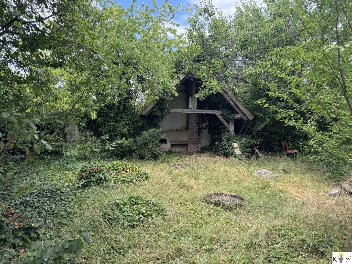Verfallenes Gartenhäuschen mit Holzbalken und überwucherten Wänden, eingebettet in die Natur.