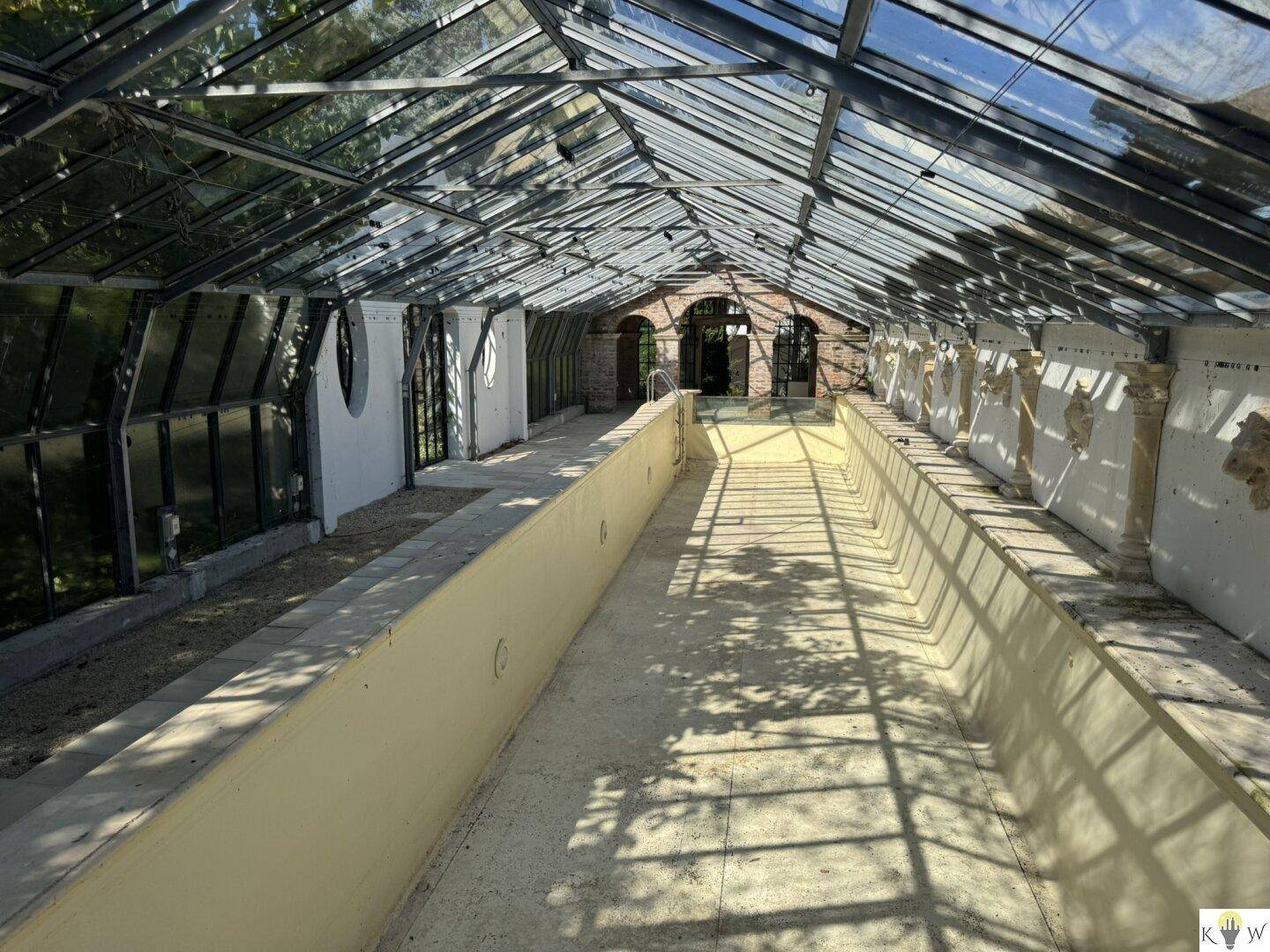 Weitläufiger, leerer Innenpool unter einem beeindruckenden Glasdach, das viel Tageslicht hereinlässt.