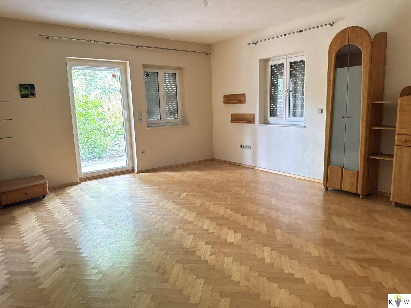Helles Wohnzimmer mit Fischgrätparkett, weiß gestrichenen Wänden und Zugang zu einem Außenbereich.