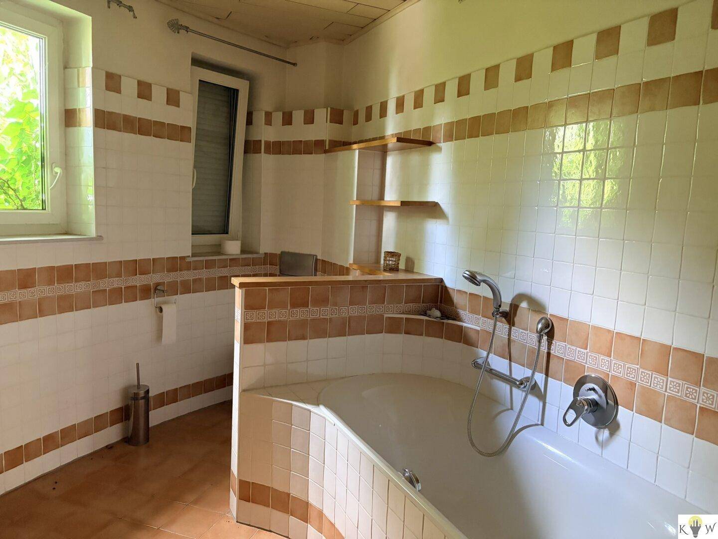 Badezimmer mit braun-weißen Fliesen, einer eingebauten Badewanne und einem Fenster, das Tageslicht spendet.