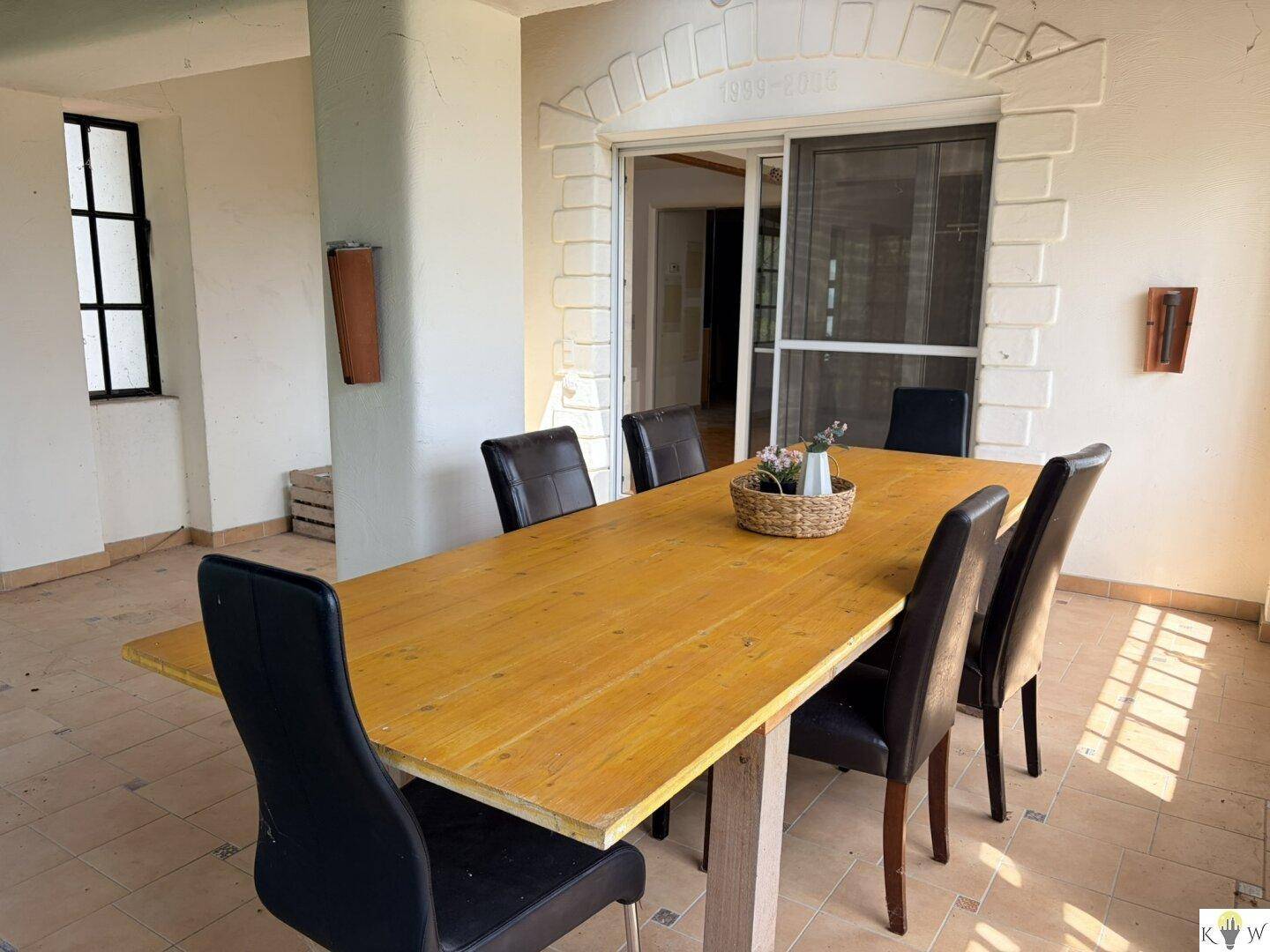 Überdachter Essbereich im Freien mit Fliesenboden und großem Holztisch, ideal für Mahlzeiten im Grünen.