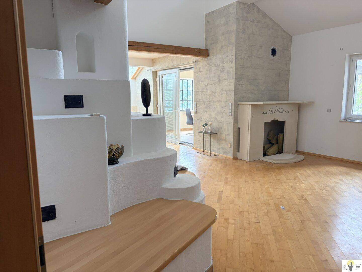 Helles Wohnzimmer mit Holzboden, einem dekorativen Kamin und großen Fenstern, die viel Licht hereinlassen.