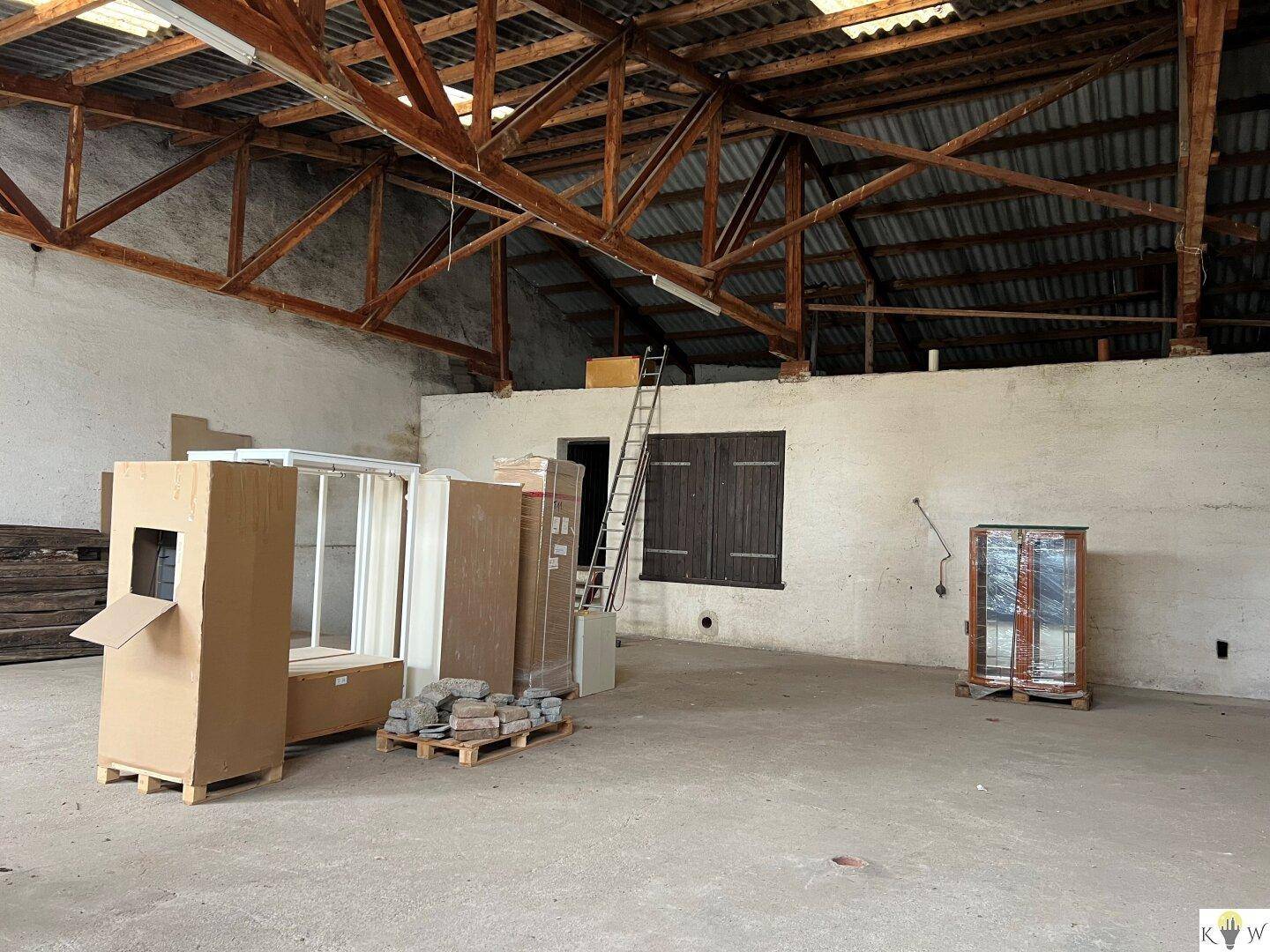 Geräumiger Innenraum einer Lagerhalle mit Holzdachstuhl und einigen gelagerten Gegenständen.