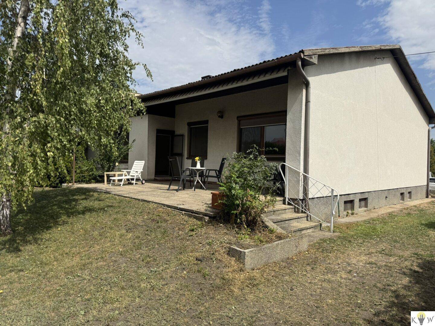 Hausfassade mit Terrasse und Treppe zum Garten, umgeben von gepflegtem Grün.