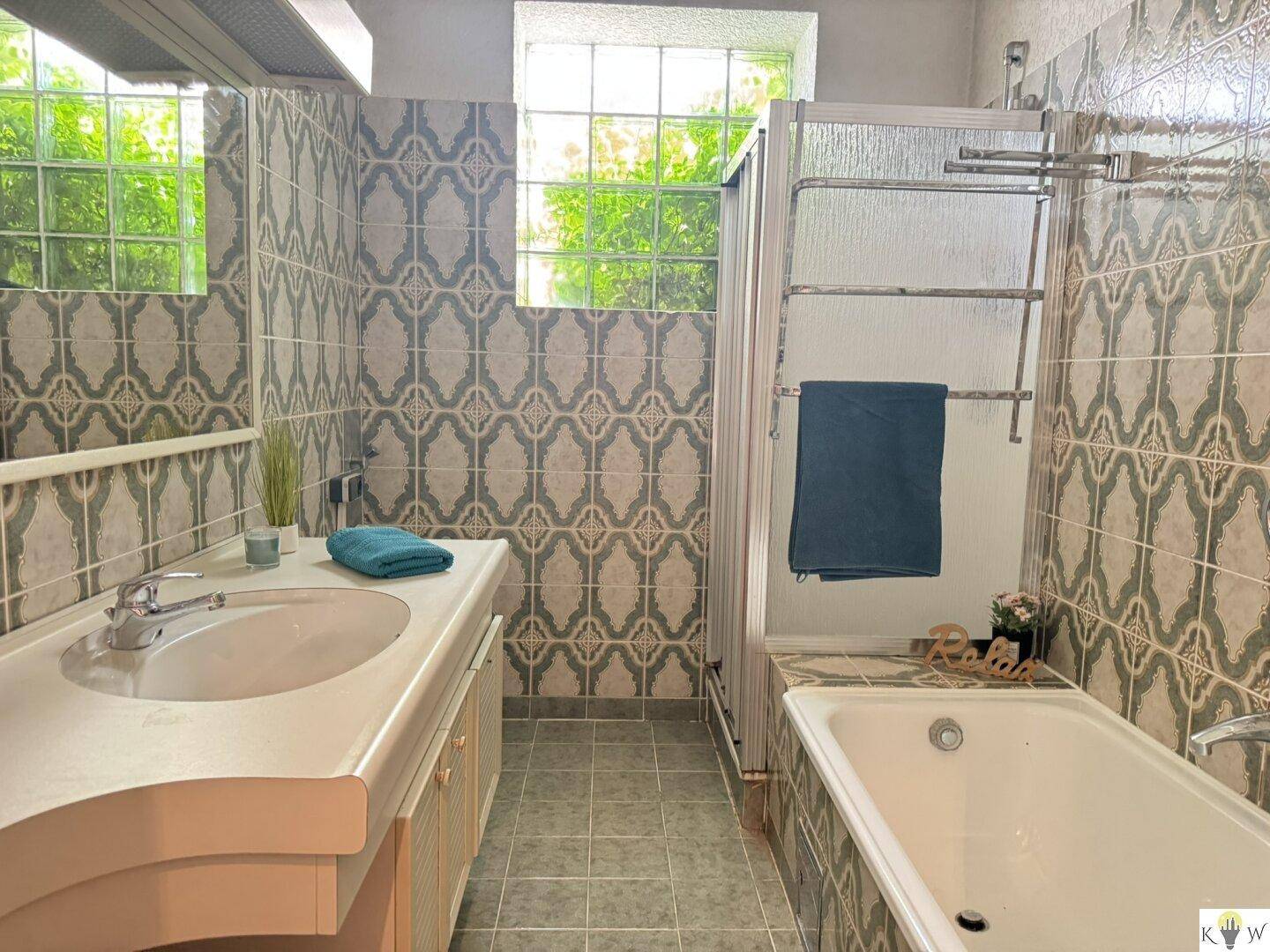 Badezimmer im Stil der 80er Jahre mit gemusterten Fliesen, Badewanne und Waschtisch.