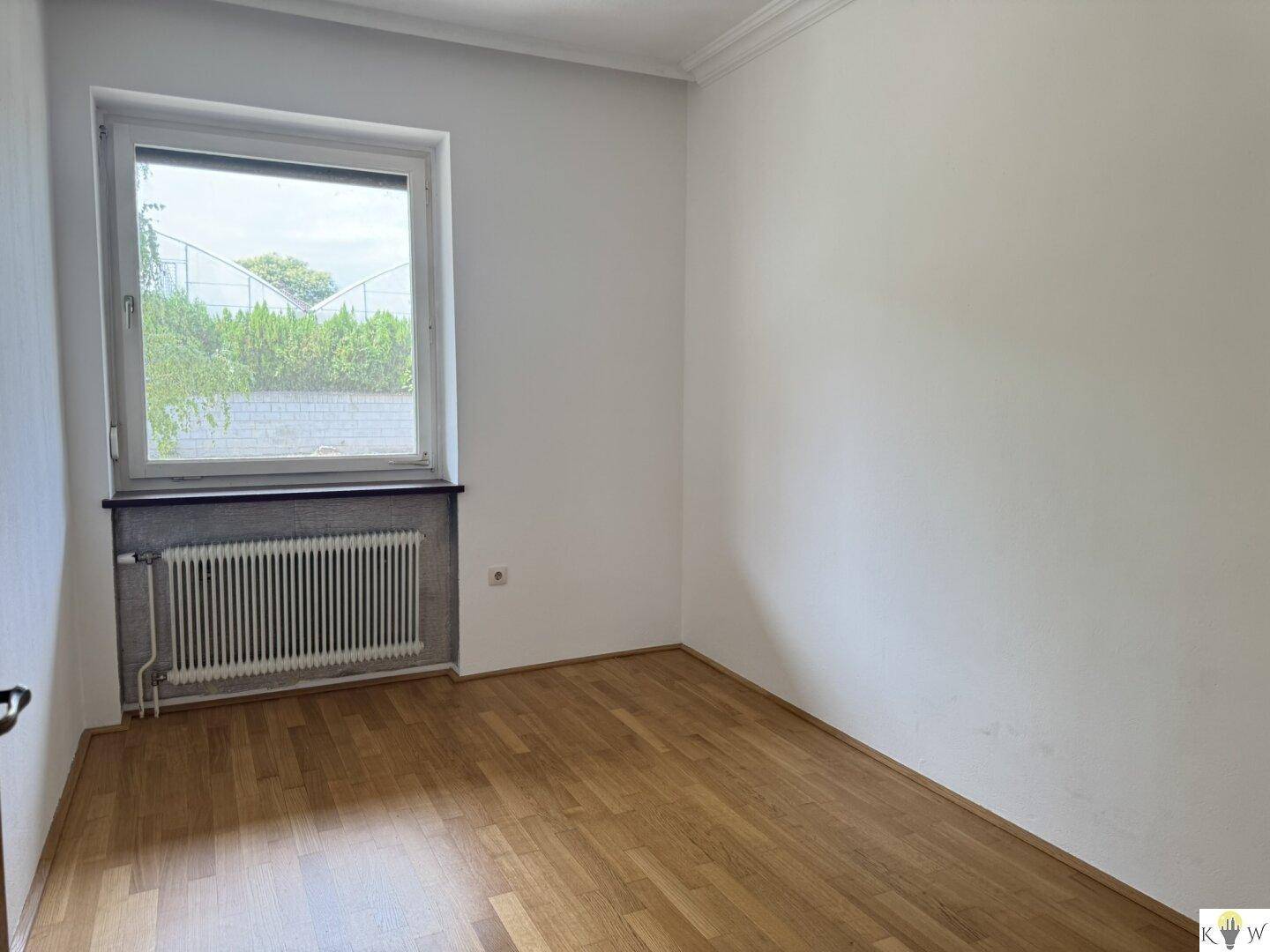Leeres Zimmer mit Parkettboden und Fenster, das vielseitig als Schlaf- oder Arbeitszimmer genutzt werden kann.
