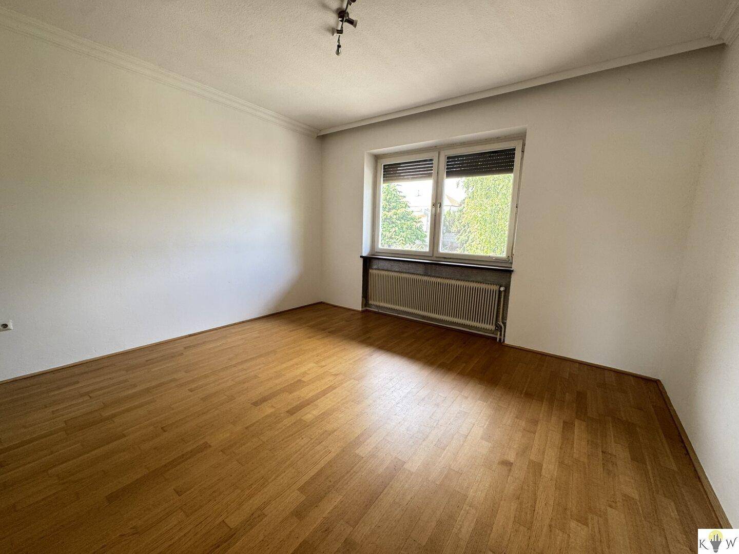 Geräumiges Wohnzimmer mit Parkettboden und großem Fenster, bereit für individuelle Gestaltung.