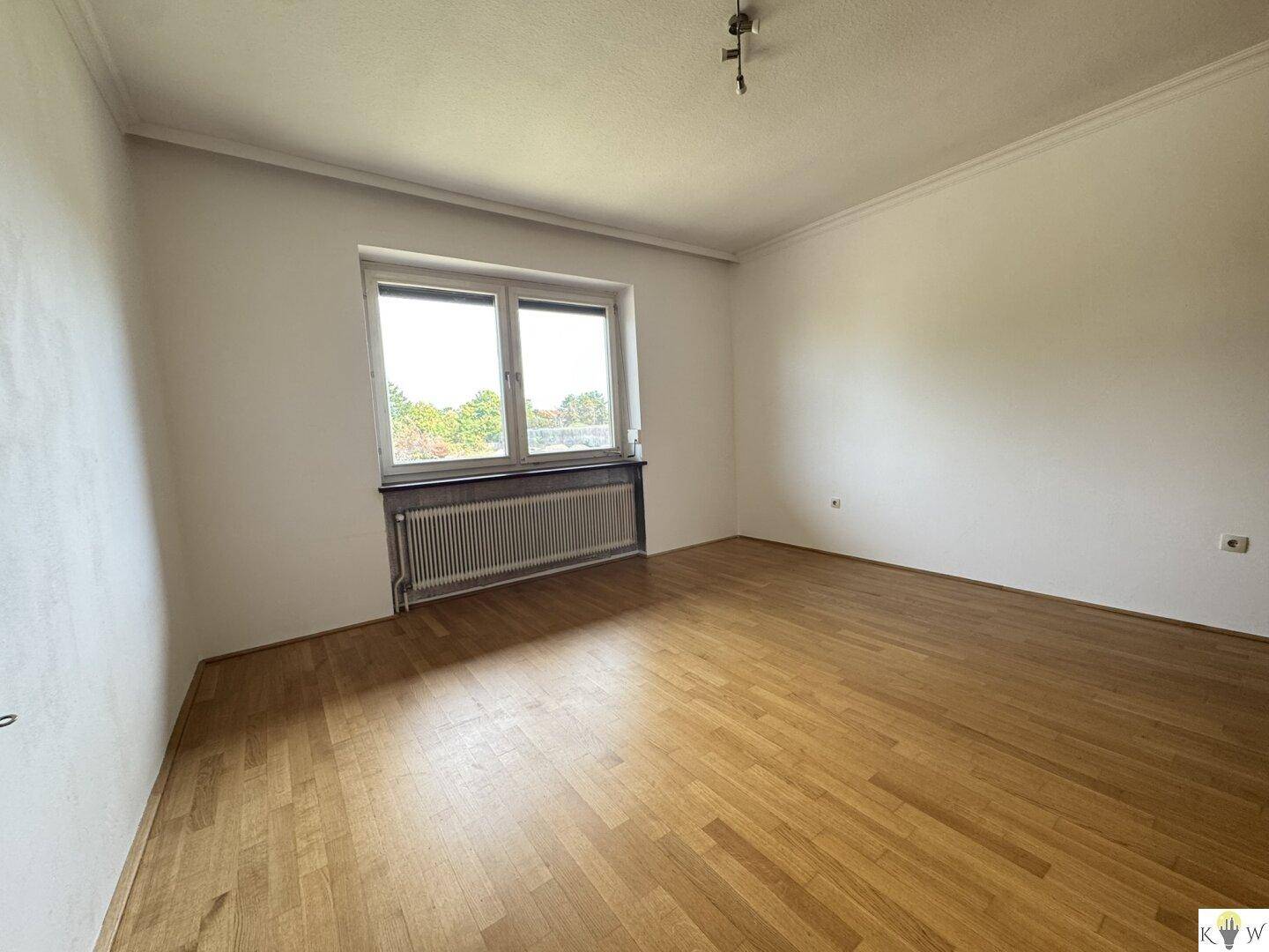 Helles Wohnzimmer mit Parkettboden und breitem Fenster, das viel Tageslicht hereinlässt.