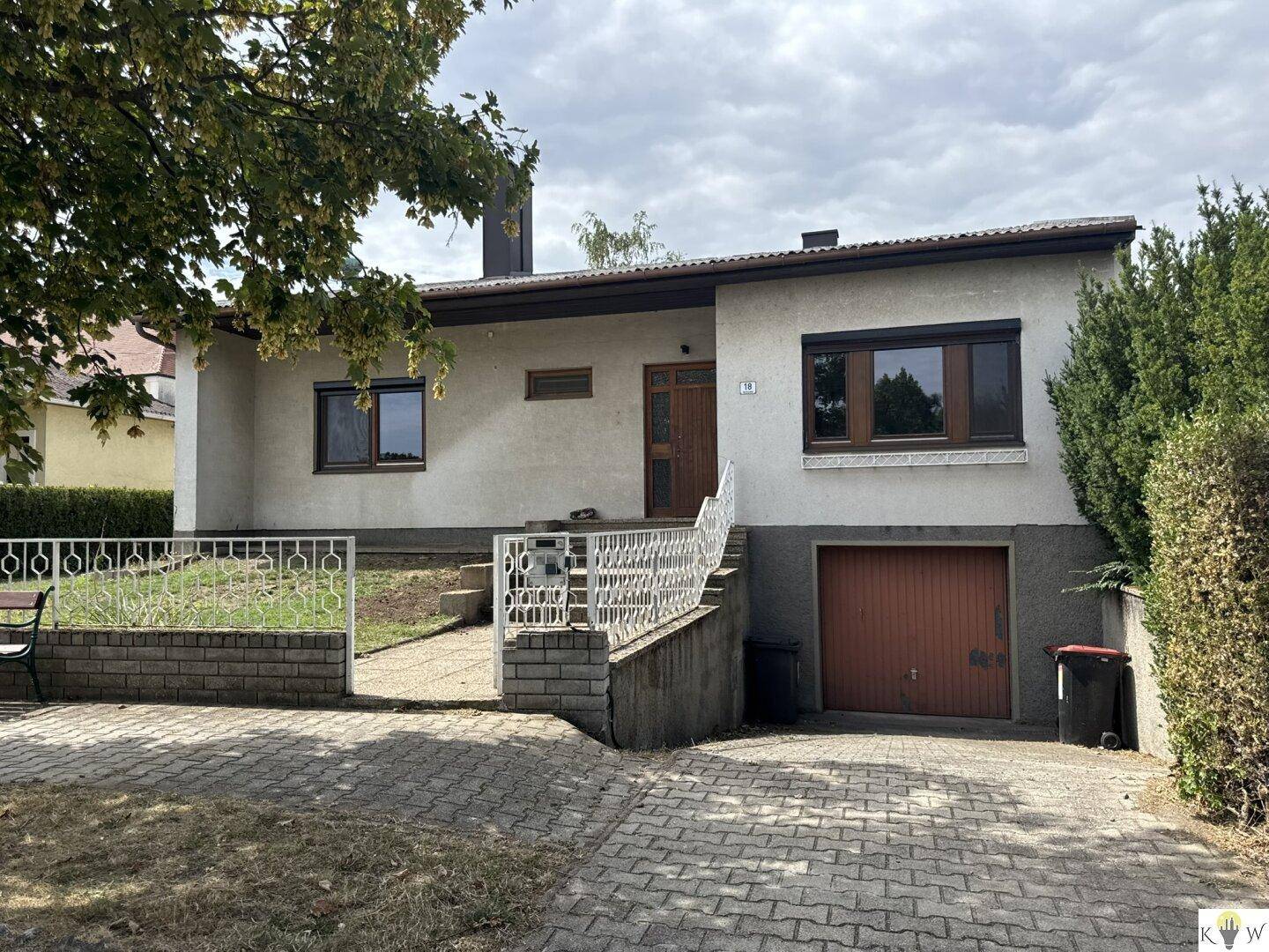 Vorderansicht des Hauses mit Auffahrt, Garage und gepflegtem Vorgarten unter bewölktem Himmel.