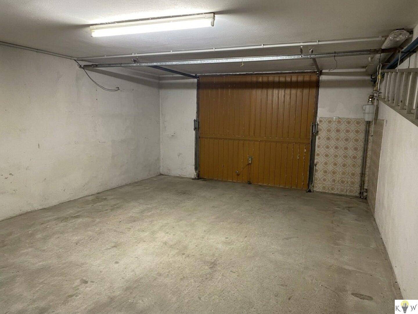 Geräumige Garage mit Betonboden und großem Tor, bietet viel Platz für Fahrzeuge und Lagerung.