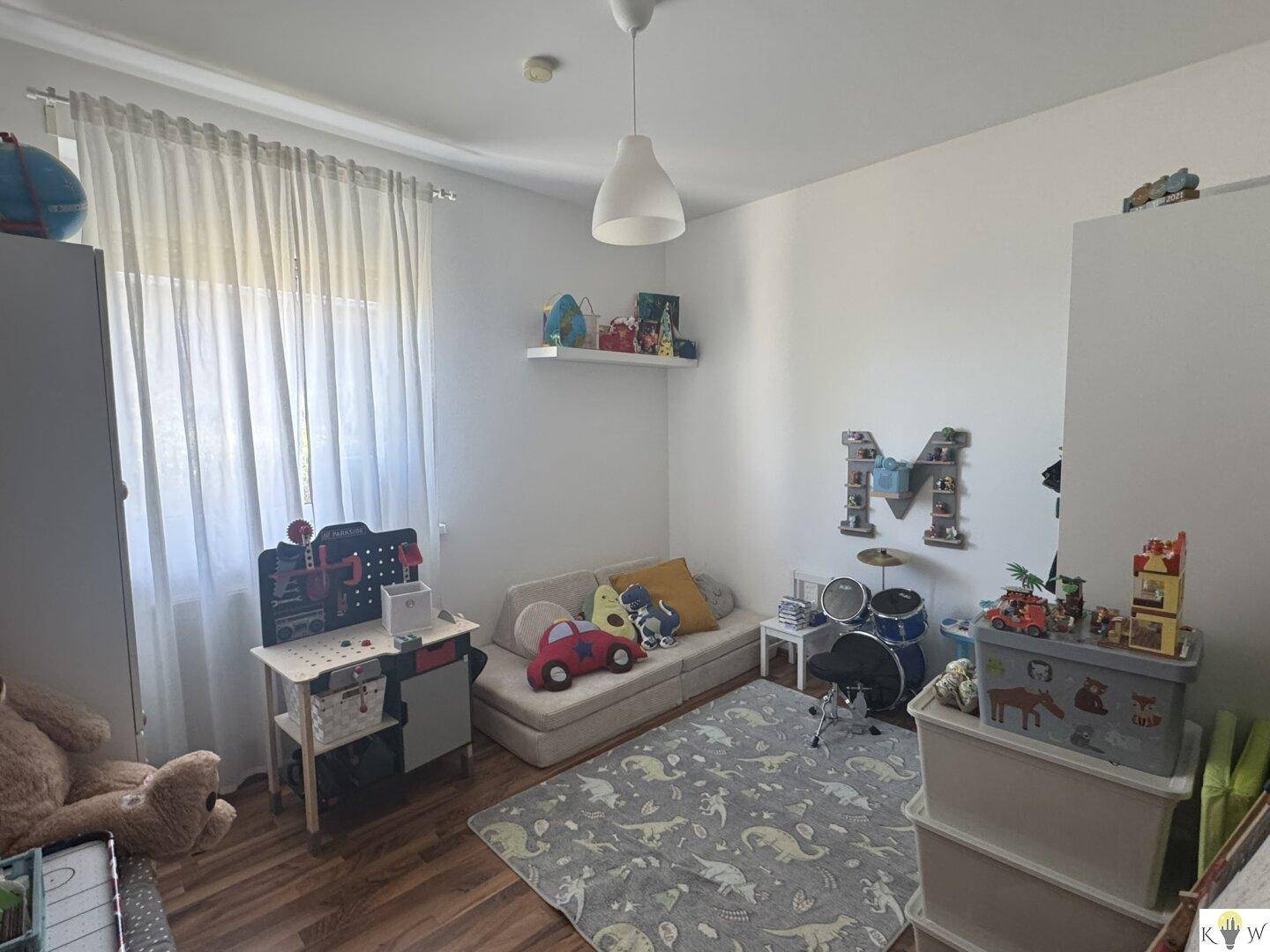 Kinderzimmer mit Spielzeug, einem kleinen Sofa und hellem Fenster, ideal für junge Bewohner.