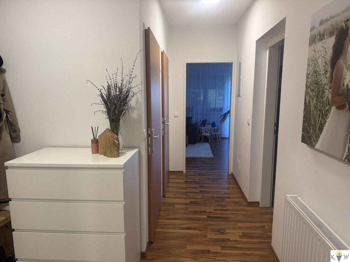 Heller Flur mit Holzboden, Kommode und Zugang zu weiteren Wohnbereichen.