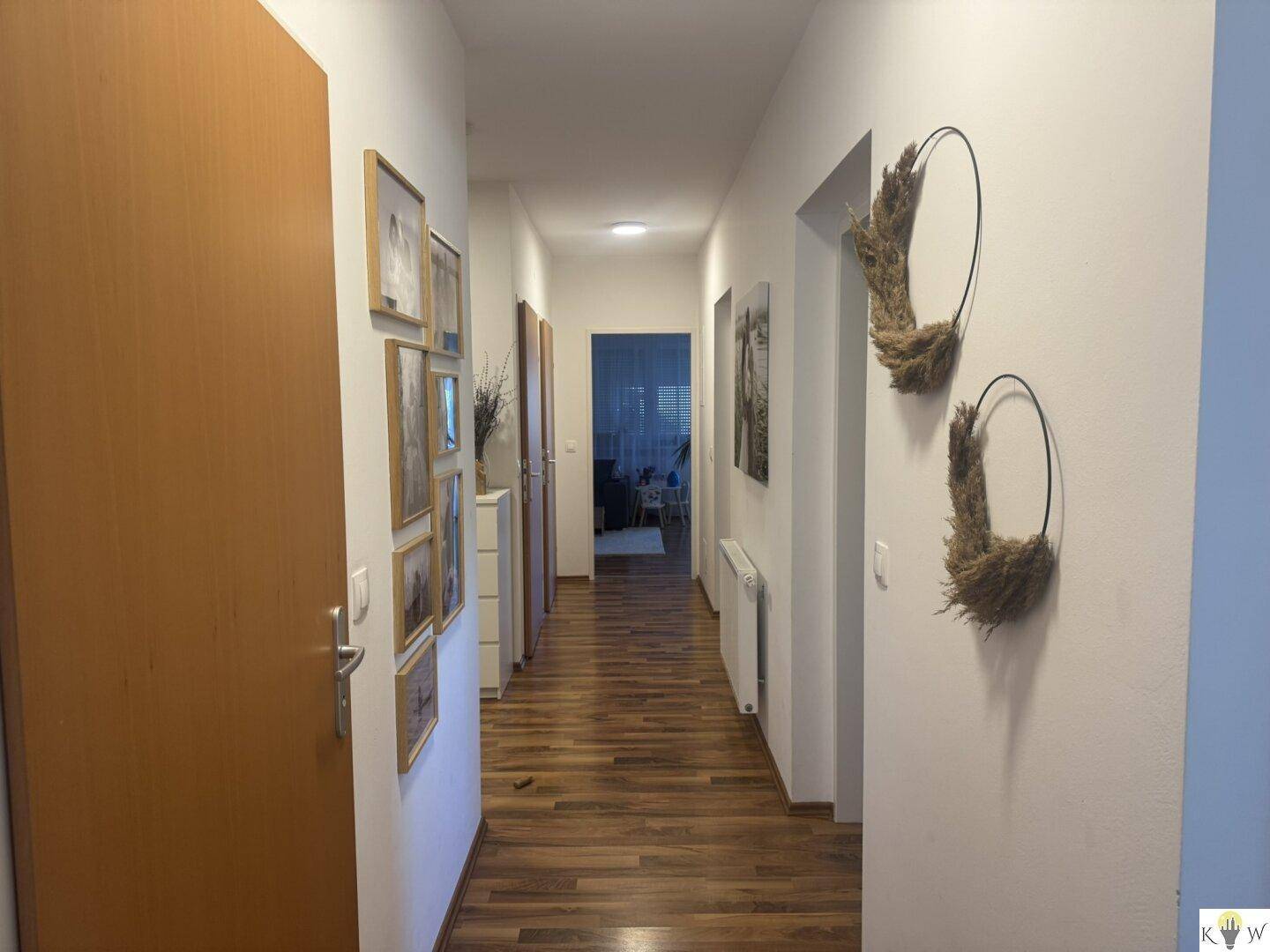 Langer Flur mit Holzboden und gerahmten Bildern an den Wänden, führt zu weiteren Räumen.