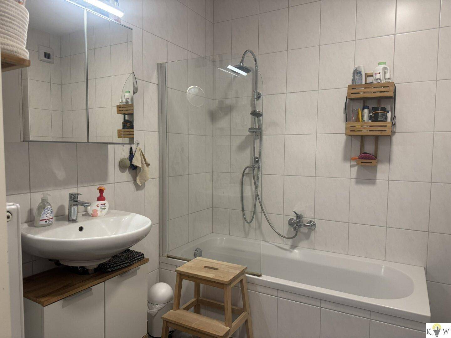 Modernes Badezimmer mit Badewanne, Duschfunktion und Waschbecken, hell gefliest.