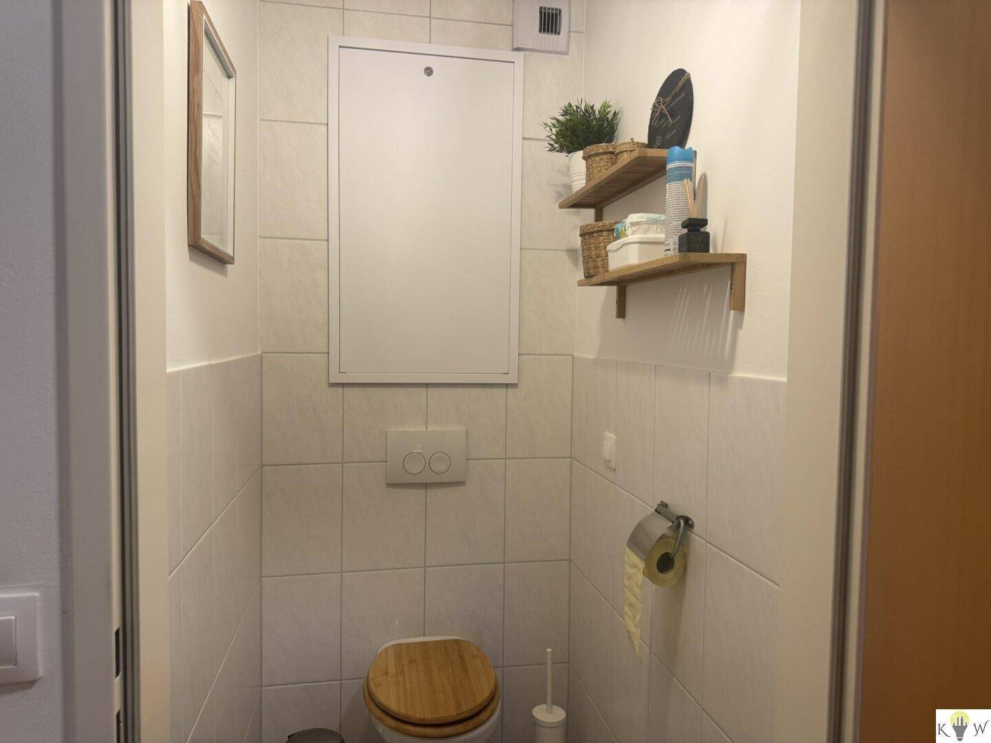 Separates WC mit Wand-WC und kleinem Waschbecken, hell gefliest.