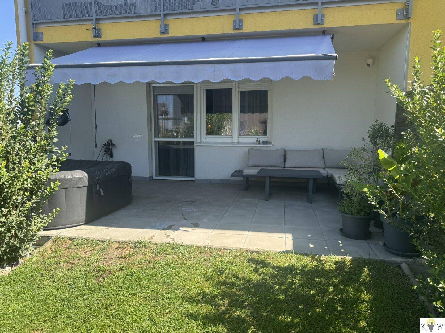 Sonniger Terrassenbereich mit Outdoor-Sofa und Whirlpool im Garten.