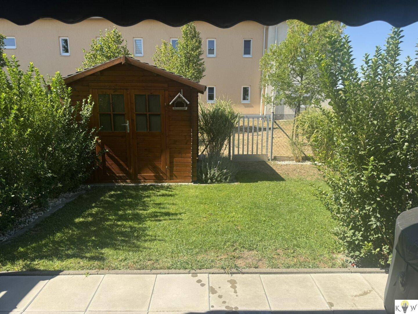 Gepflegter Gartenbereich mit Rasenfläche, Gartenhaus und Hecken, umzäunt.