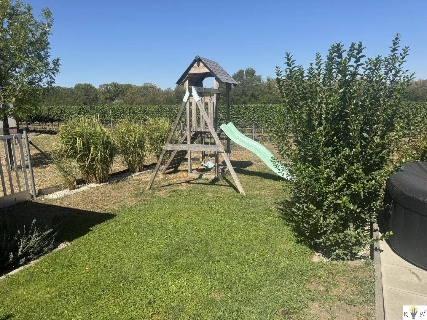 Großer Garten mit Kinderspielturm, Rutsche und Whirlpool, umgeben von Grün.