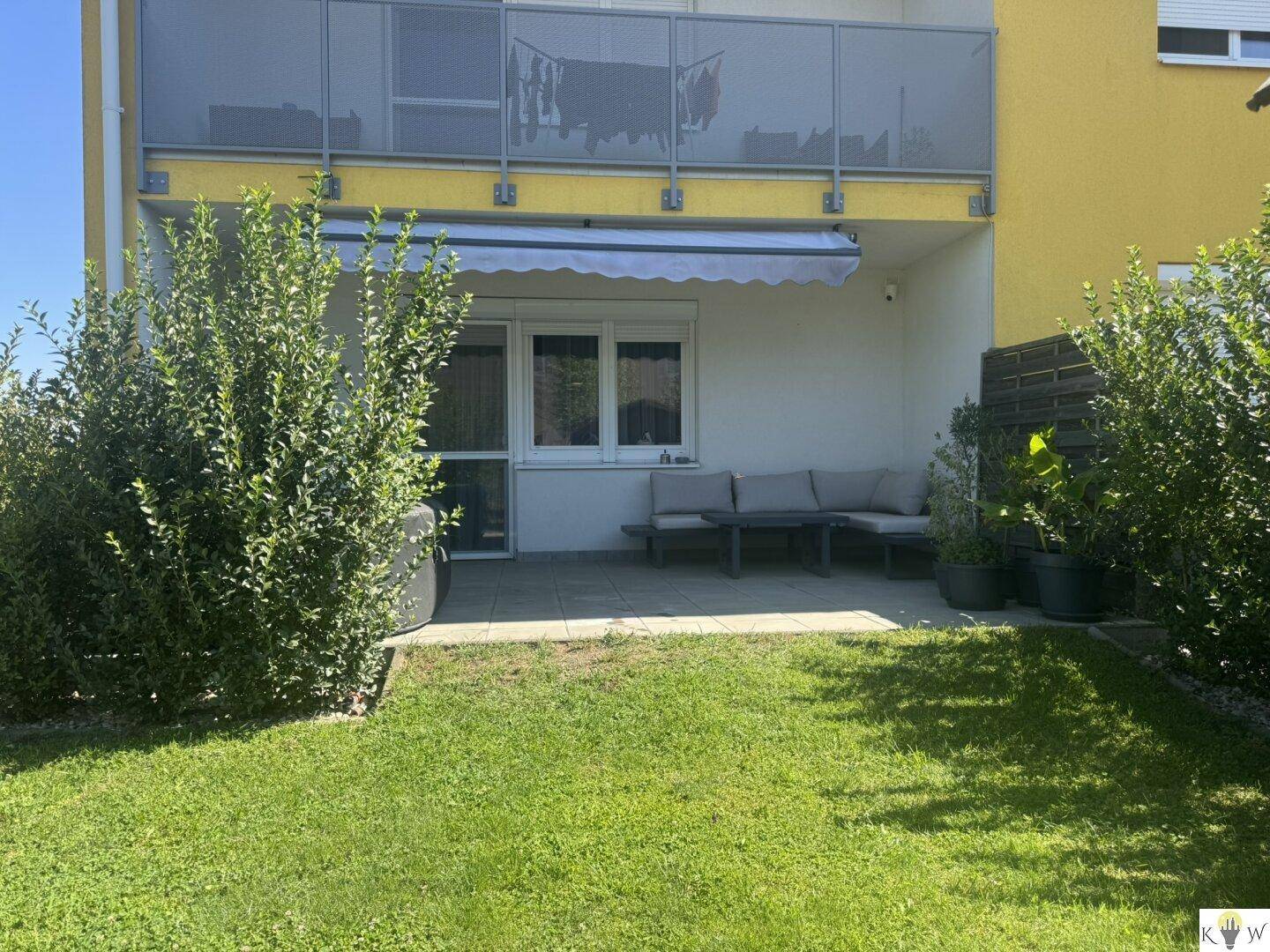Sonniger Terrassenbereich mit Sitzgelegenheiten und angrenzendem Rasen im Garten.