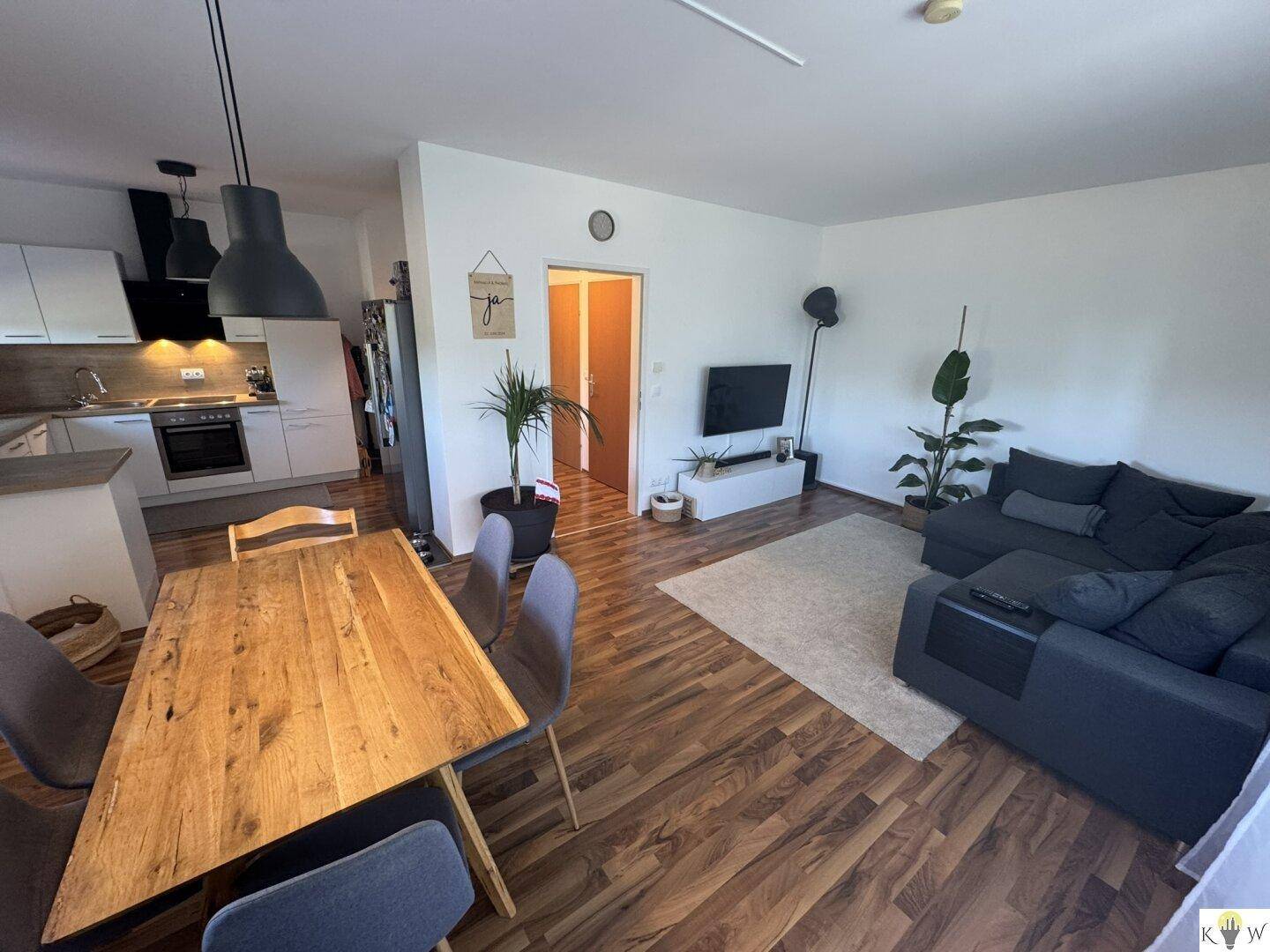 Geräumiger Wohn- und Essbereich mit Sofa, Fernseher und offener Verbindung zur Küche.