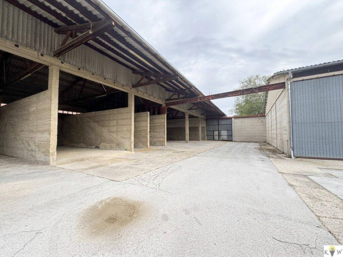 Überdachter Lagerbereich mit Betonwänden, Wellblechdach und sichtbaren Holzbalken, ideal für industrielle Nutzung.