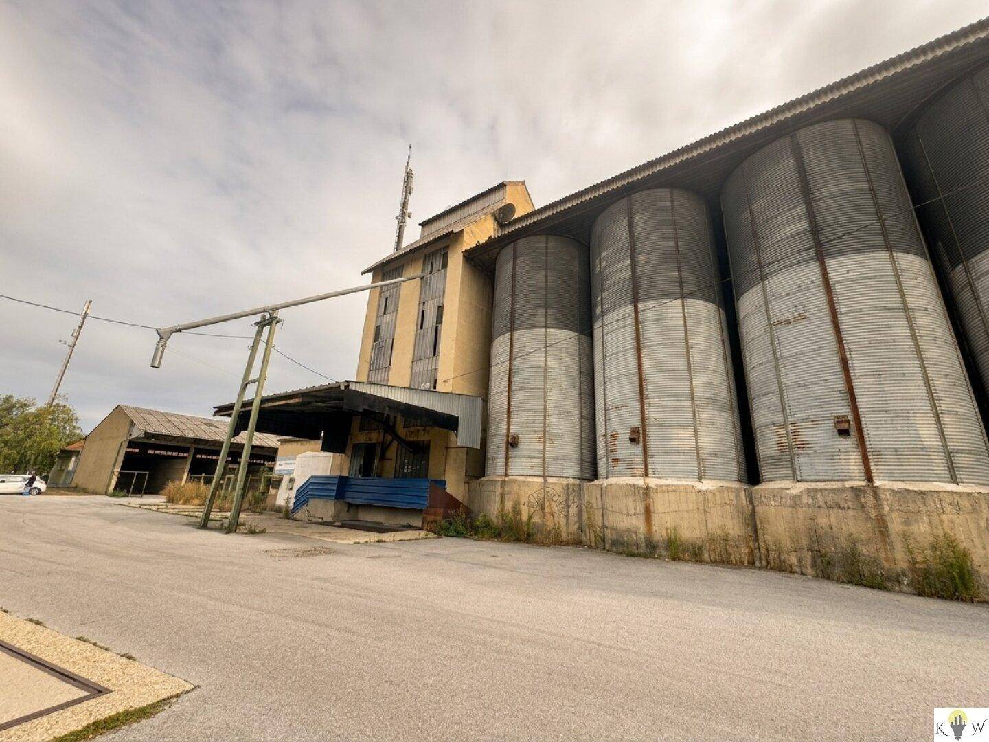 Industriekomplex mit hohen Getreidesilos, Förderanlagen und einem Mobilfunkmast unter bewölktem Himmel.