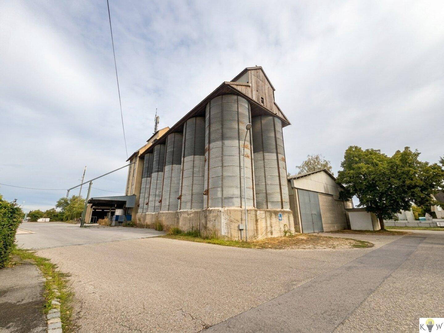 Großer Industriekomplex mit markanten Silos und einem angrenzenden Gebäude, umgeben von Grünflächen.