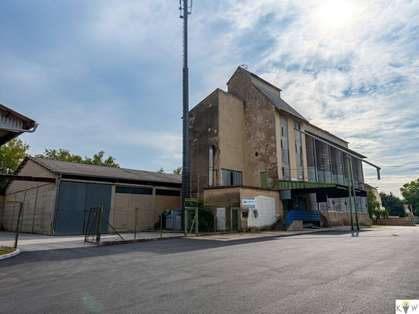 Industrielles Gebäude mit einer robusten Fassade, einem Mobilfunkmast und einem großen asphaltierten Vorplatz.