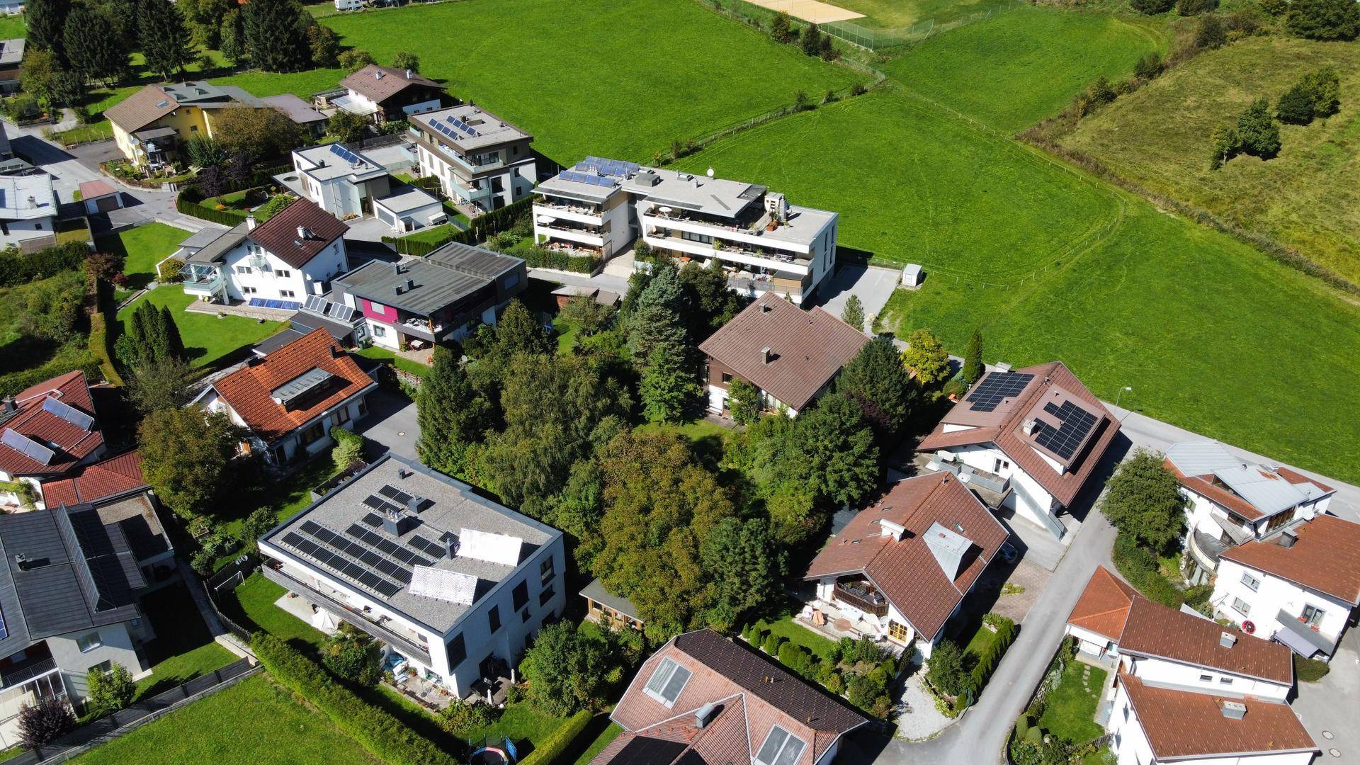 Weitläufige Luftaufnahme der Wohnsiedlung mit Einfamilienhäusern und viel Grün in bergiger Umgebung.