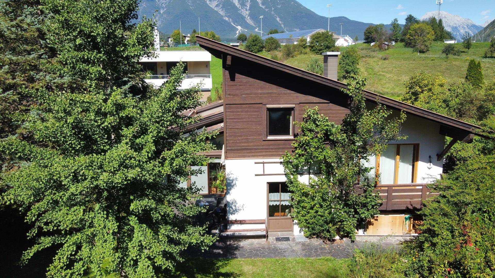 Modernes Haus mit Holzfassade und schrägem Dach, umgeben von üppigem Grün und Bäumen.