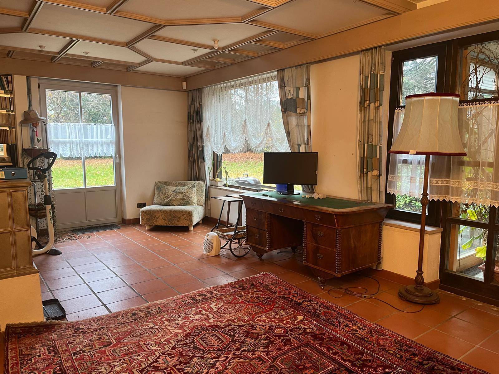 Geräumiges Wohnzimmer mit Terrakottaboden, Holzbalkendecke, Kaminofen und direktem Zugang zum Gartenbereich.