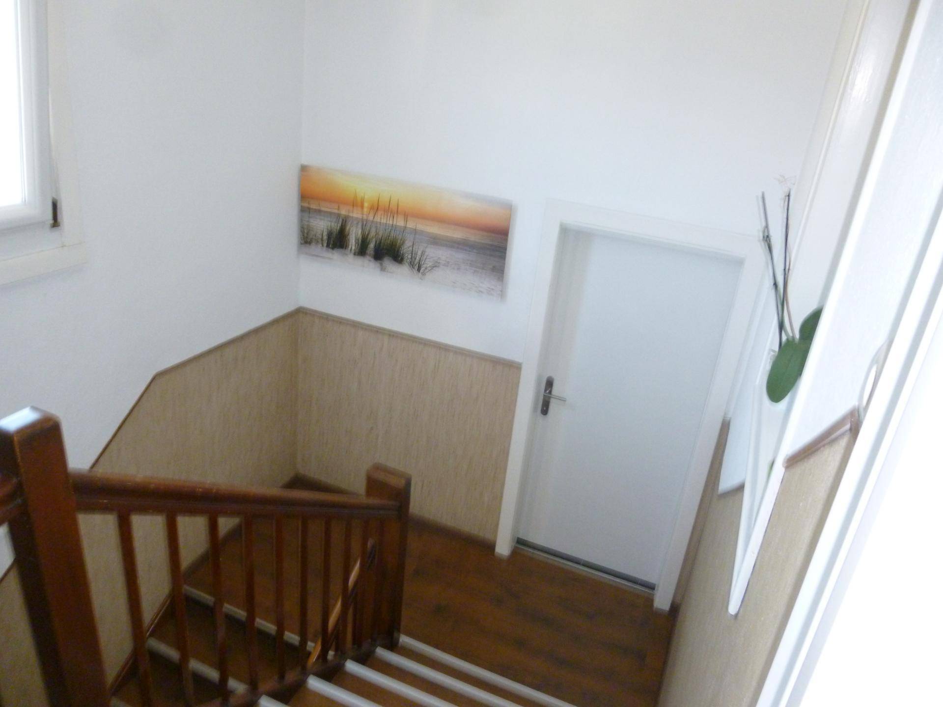 Holztreppe mit Geländer und einem Bild an der Wand, führt in die obere Etage.