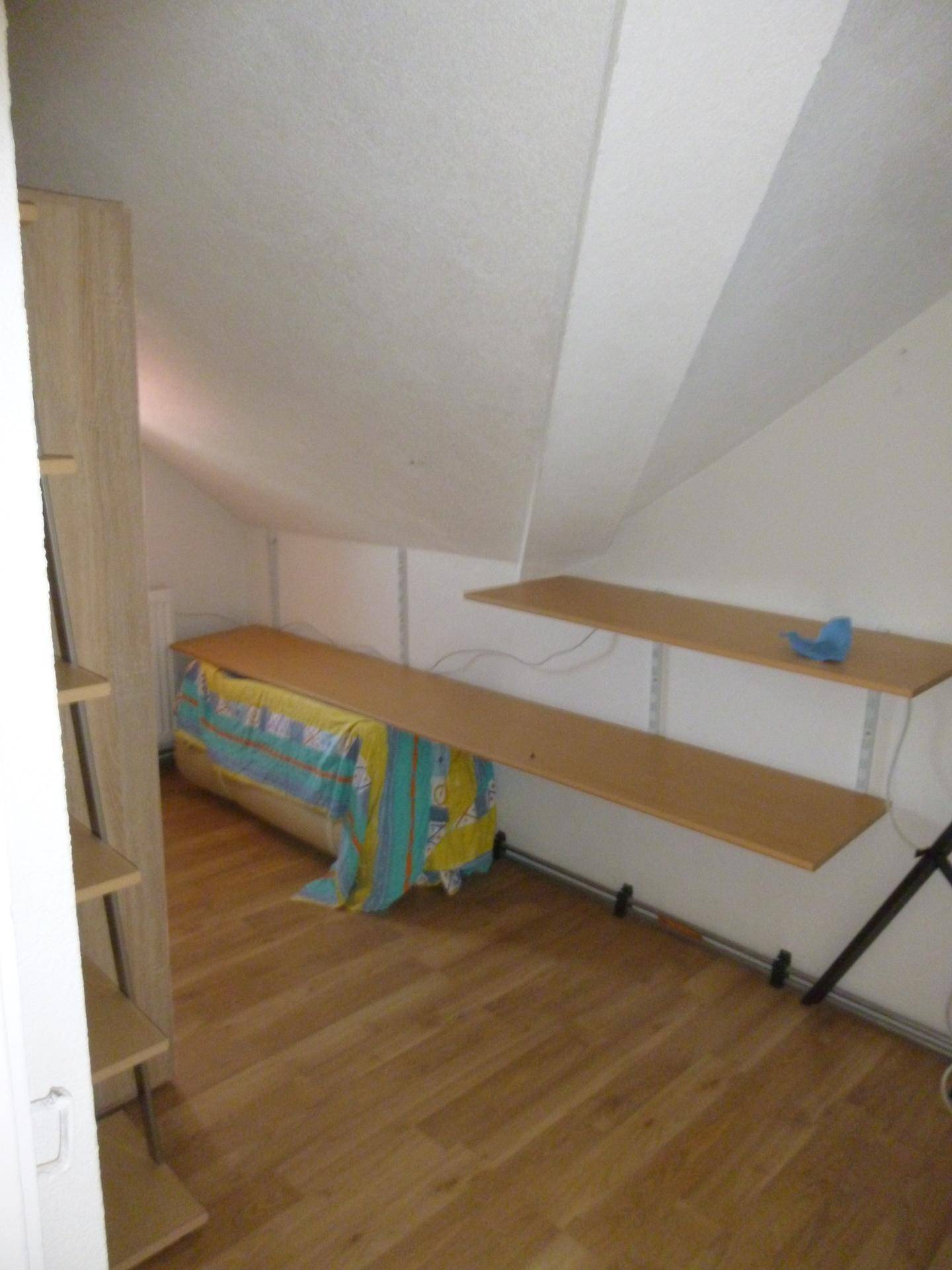 Dachzimmer mit schrägen Wänden, Laminatboden und praktischen Regalen für Stauraum.
