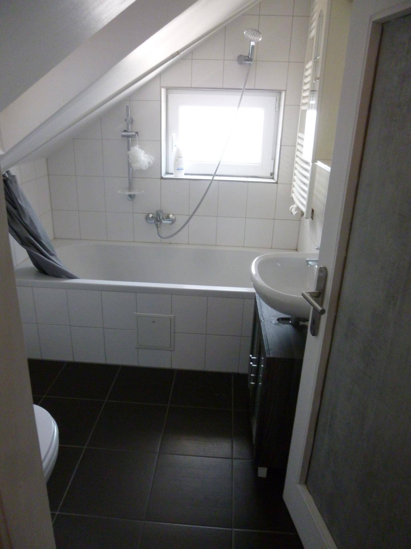 Badezimmer mit Badewanne, Waschbecken und Dachschräge, hell durch ein Fenster.