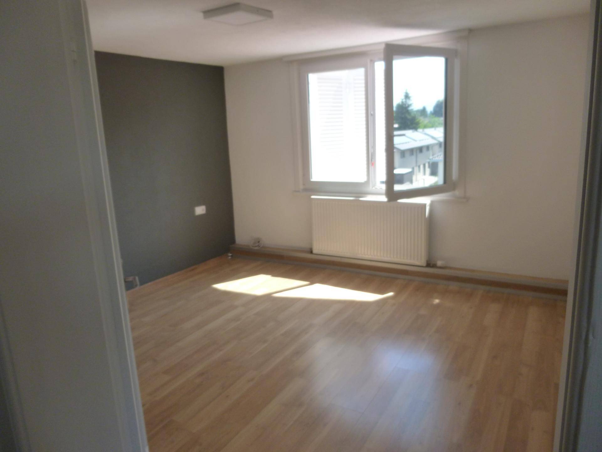 Helles Zimmer mit Laminatboden, weiß gestrichenen Wänden und einem großen Fenster.